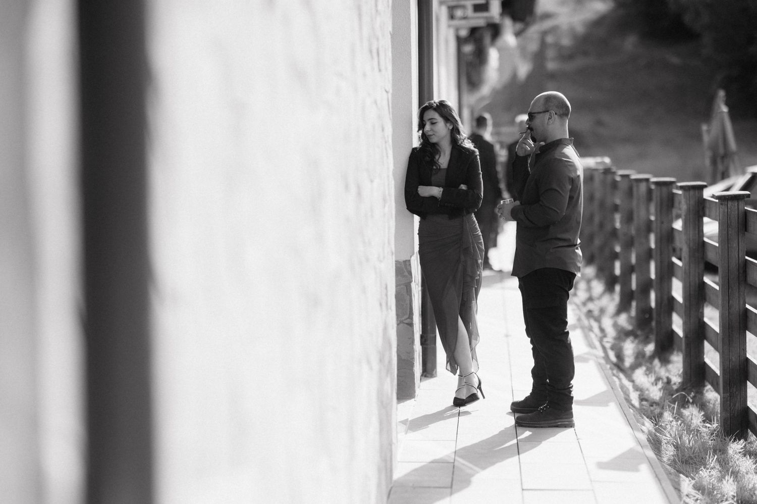 A black and white photograph shows a pensive moment on a walkway with a railing, captured in soft lighting and shadows.