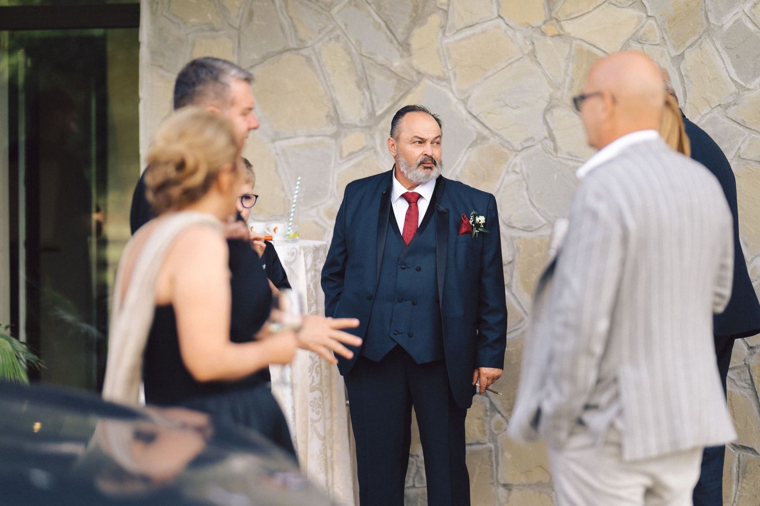Newlyweds share a close moment during their outdoor wedding reception while guests mingle in the background.