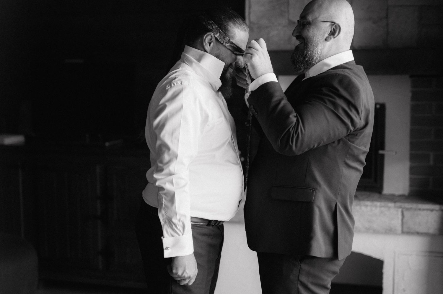 Black and white image of wedding preparation with formal attire adjustments.