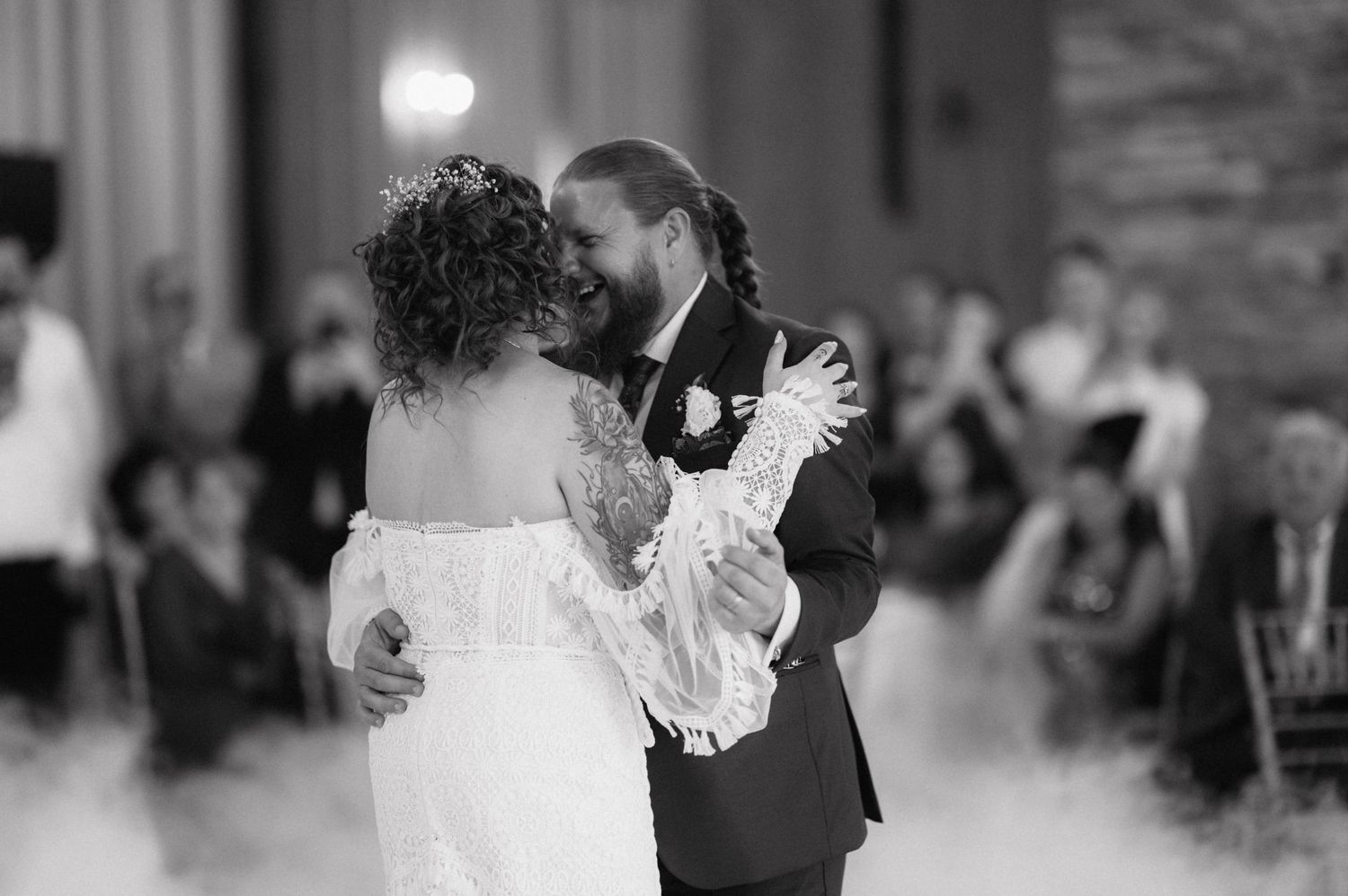 A couple sharing their first dance at a wedding reception, with other guests visible in the background.