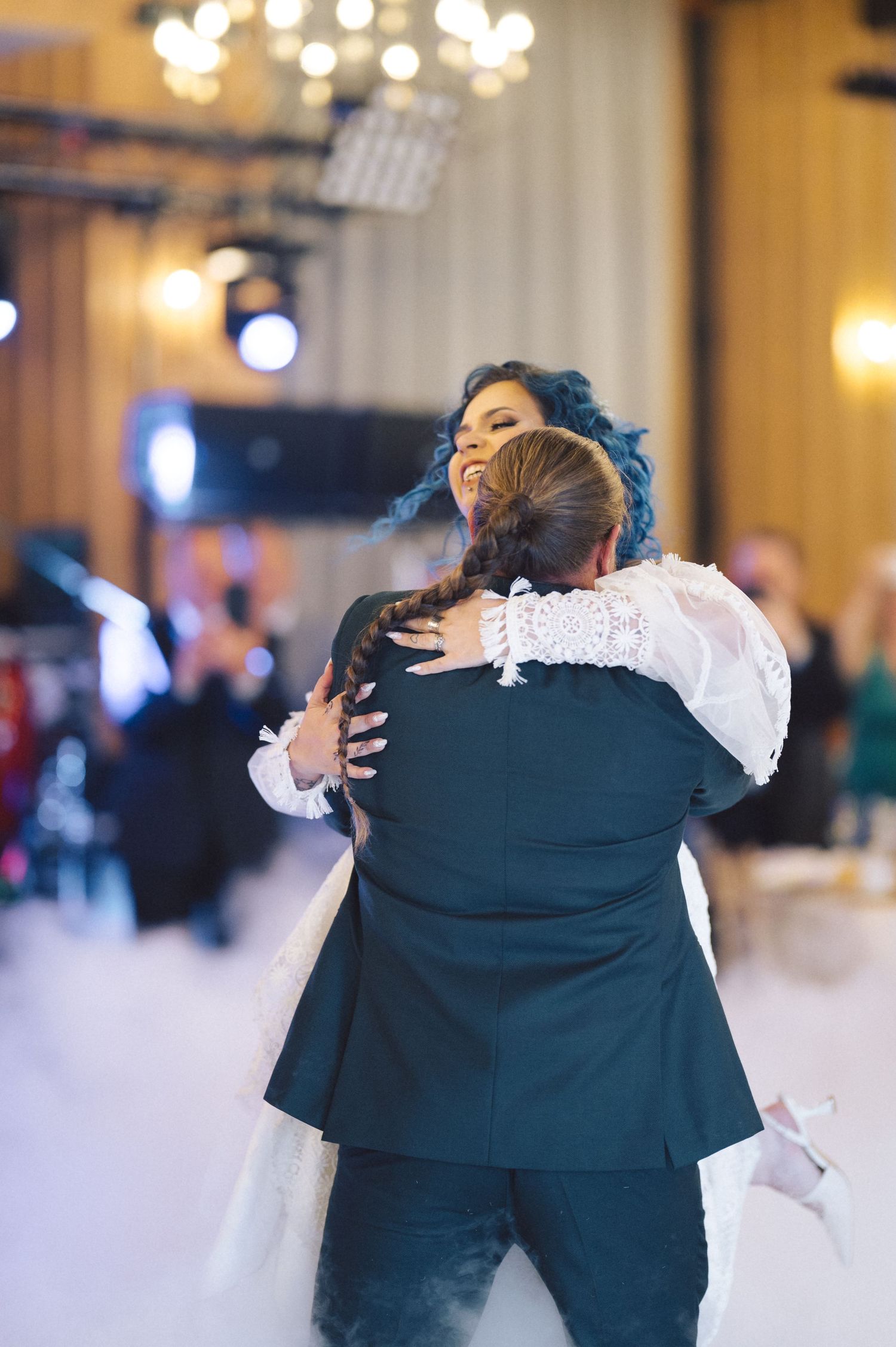 A bride and groom share an intimate embrace during their first dance at an elegant wedding reception with warm lighting.