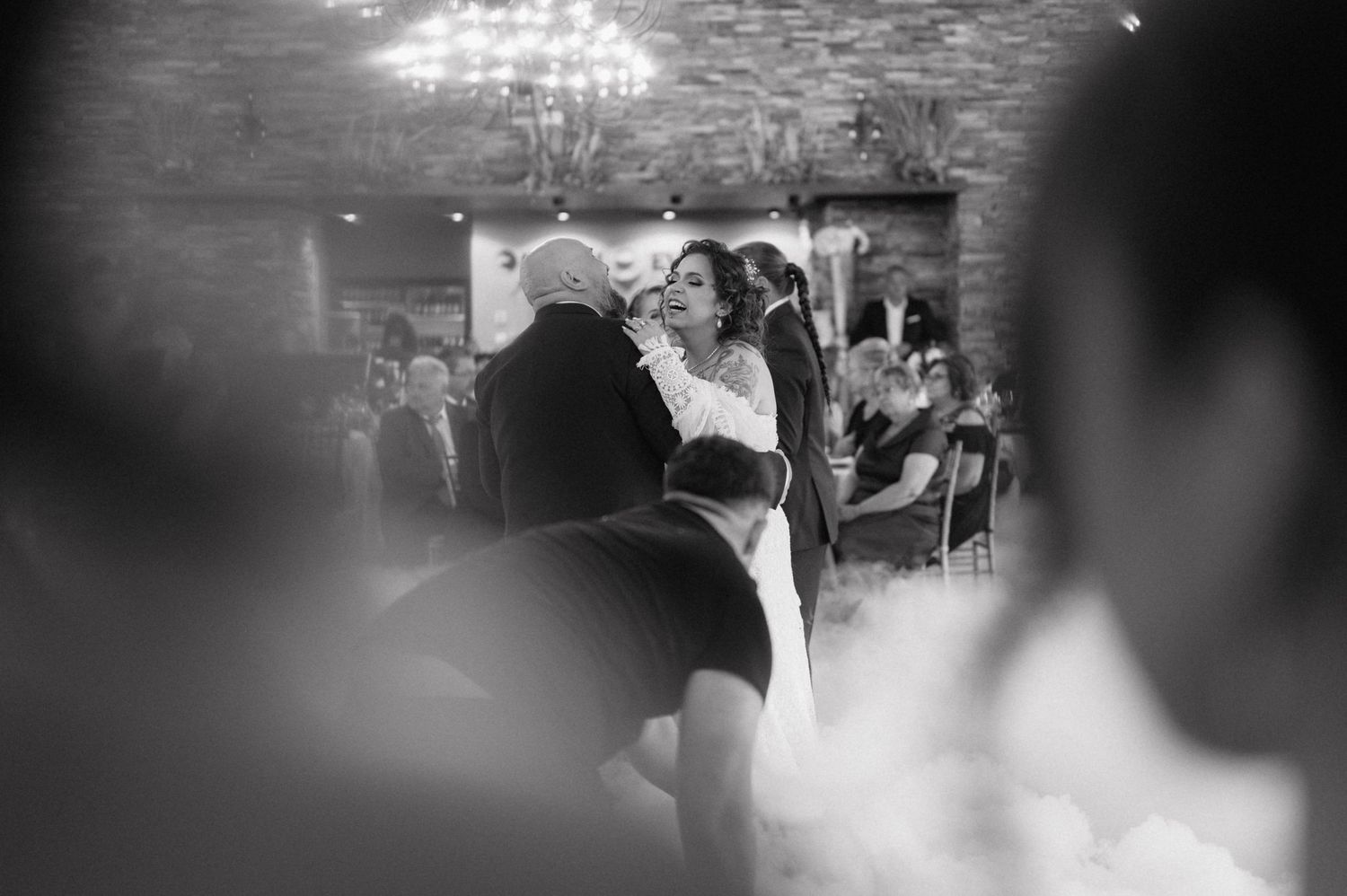 A couple shares a romantic dance at their wedding reception under glittering chandeliers in black and white photography.
