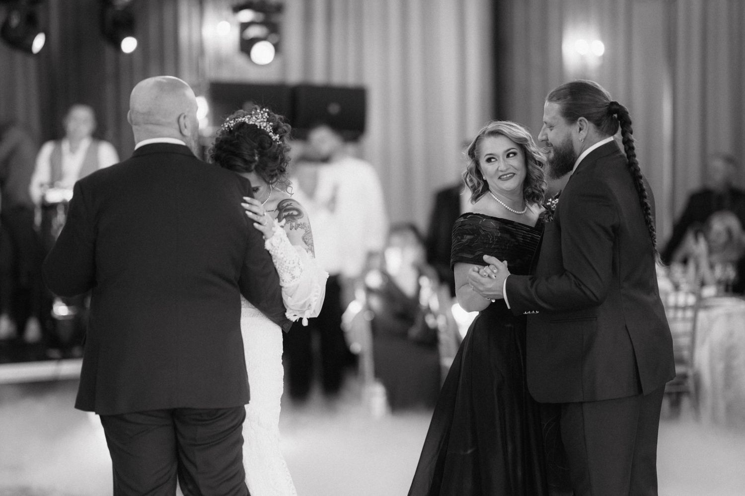 Elegant couple in formal attire dancing at an upscale black and white event with other guests on the dance floor.