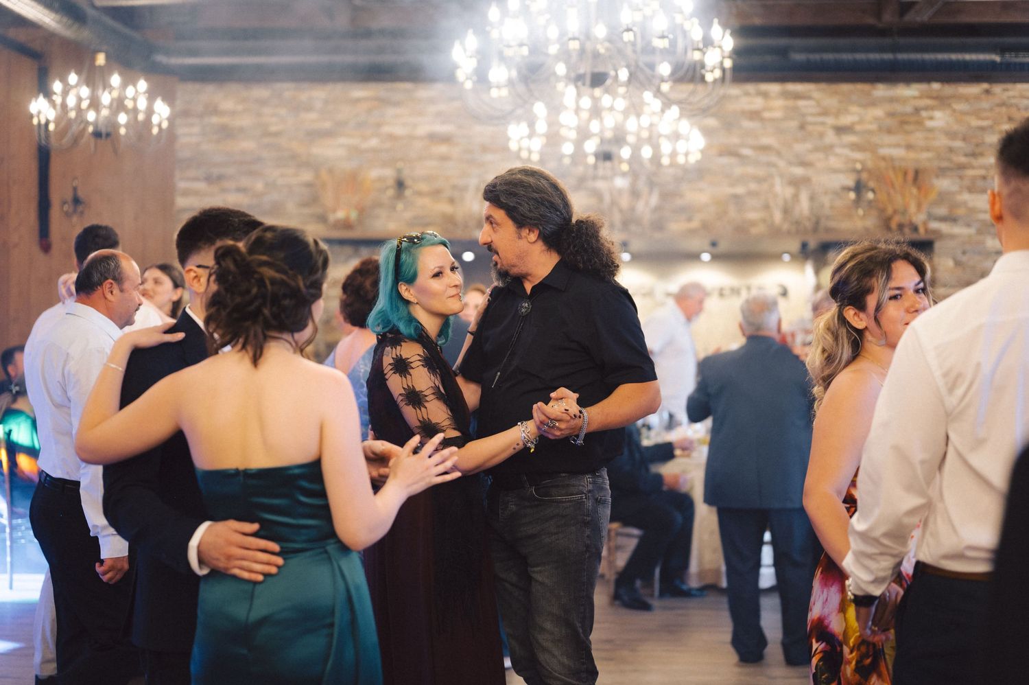 Couples dancing together during a wedding reception in an elegant venue with crystal chandeliers and exposed brick walls.