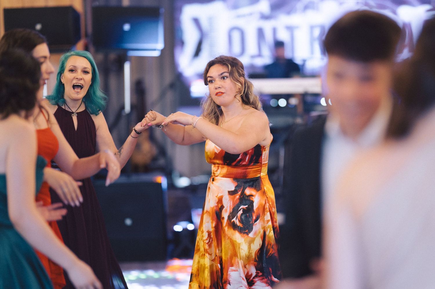 People dancing and having fun at a party with one dancer wearing a vibrant orange floral dress in focus.