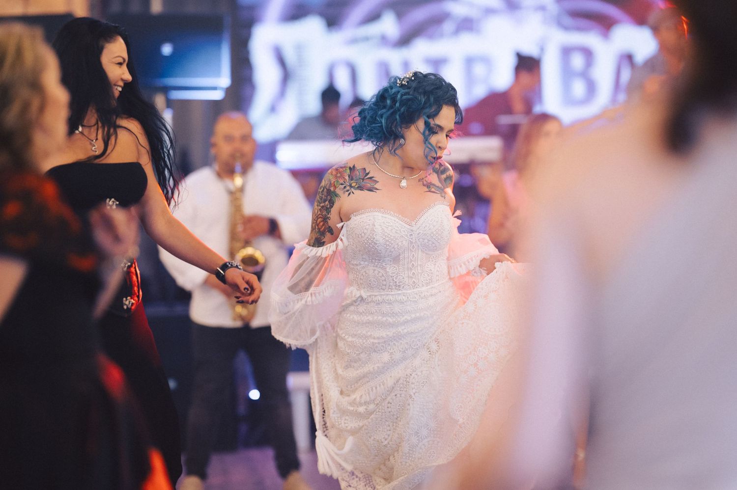 A joyful figure in a flowing white lace wedding dress dances energetically on an illuminated reception dance floor.
