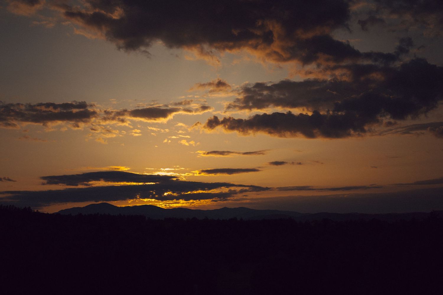 Dramatic orange sunset sky with dark silhouetted mountains and dramatic clouds during golden hour.