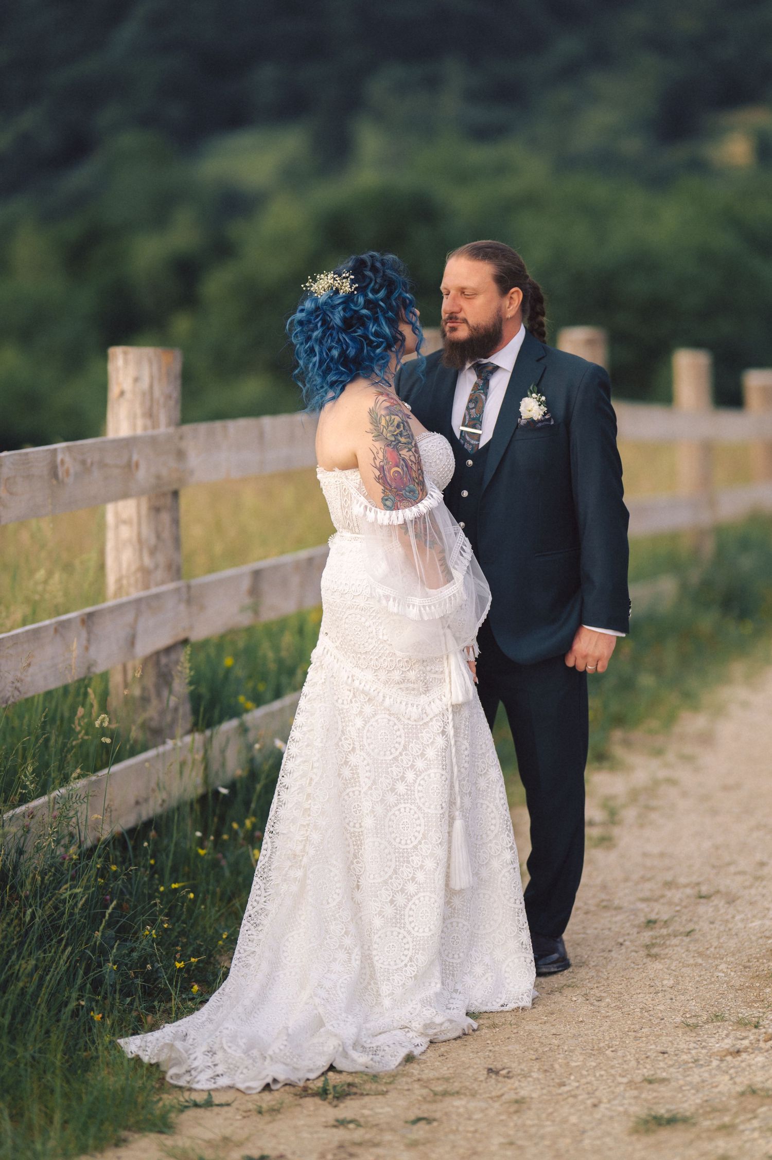A romantic wedding couple shares an intimate dance on a rustic dirt path bordered by a wooden fence at sunset.