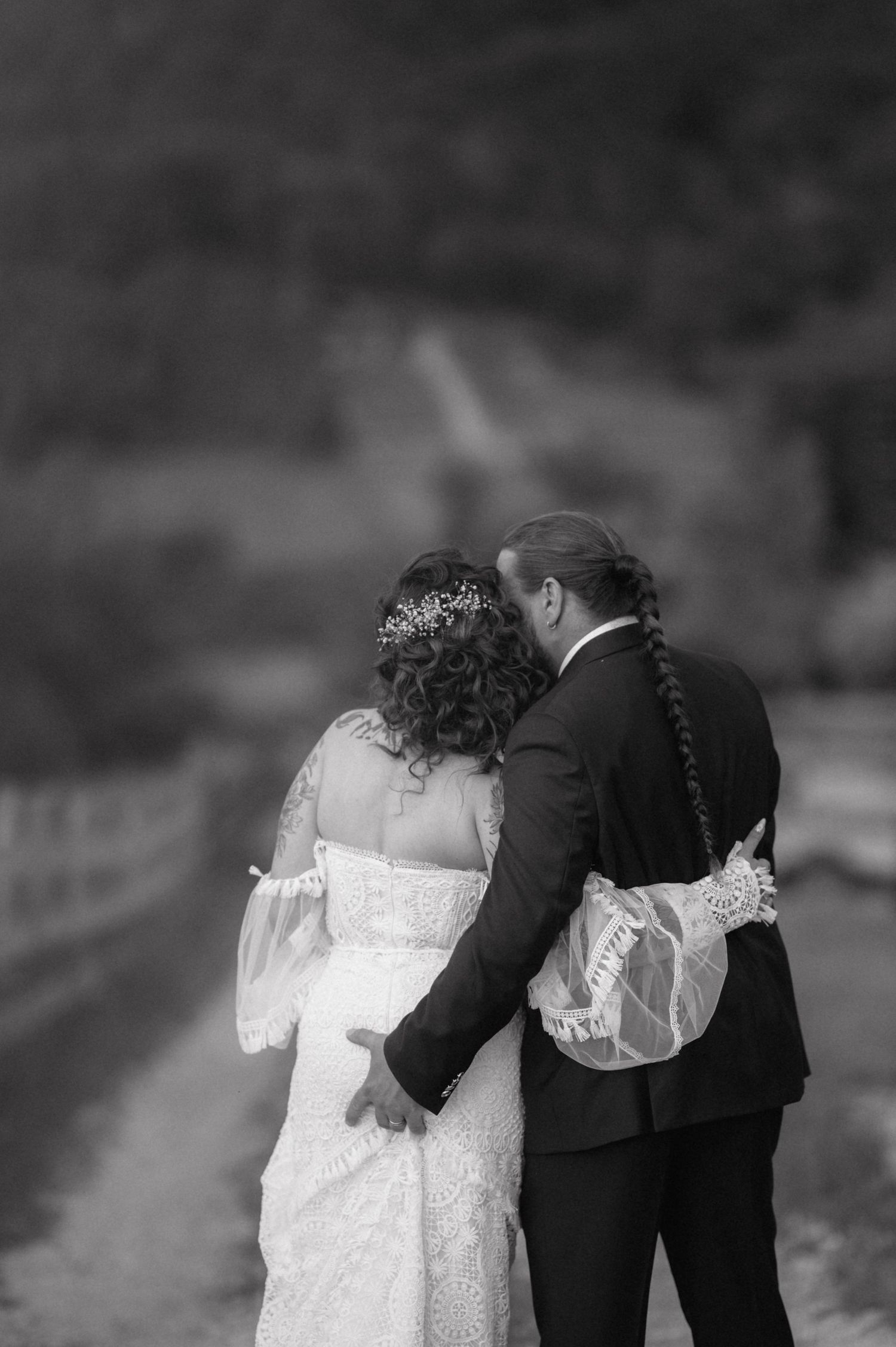 Black and white photo capturing two newlyweds from behind wearing matching lace details on their wedding attire.