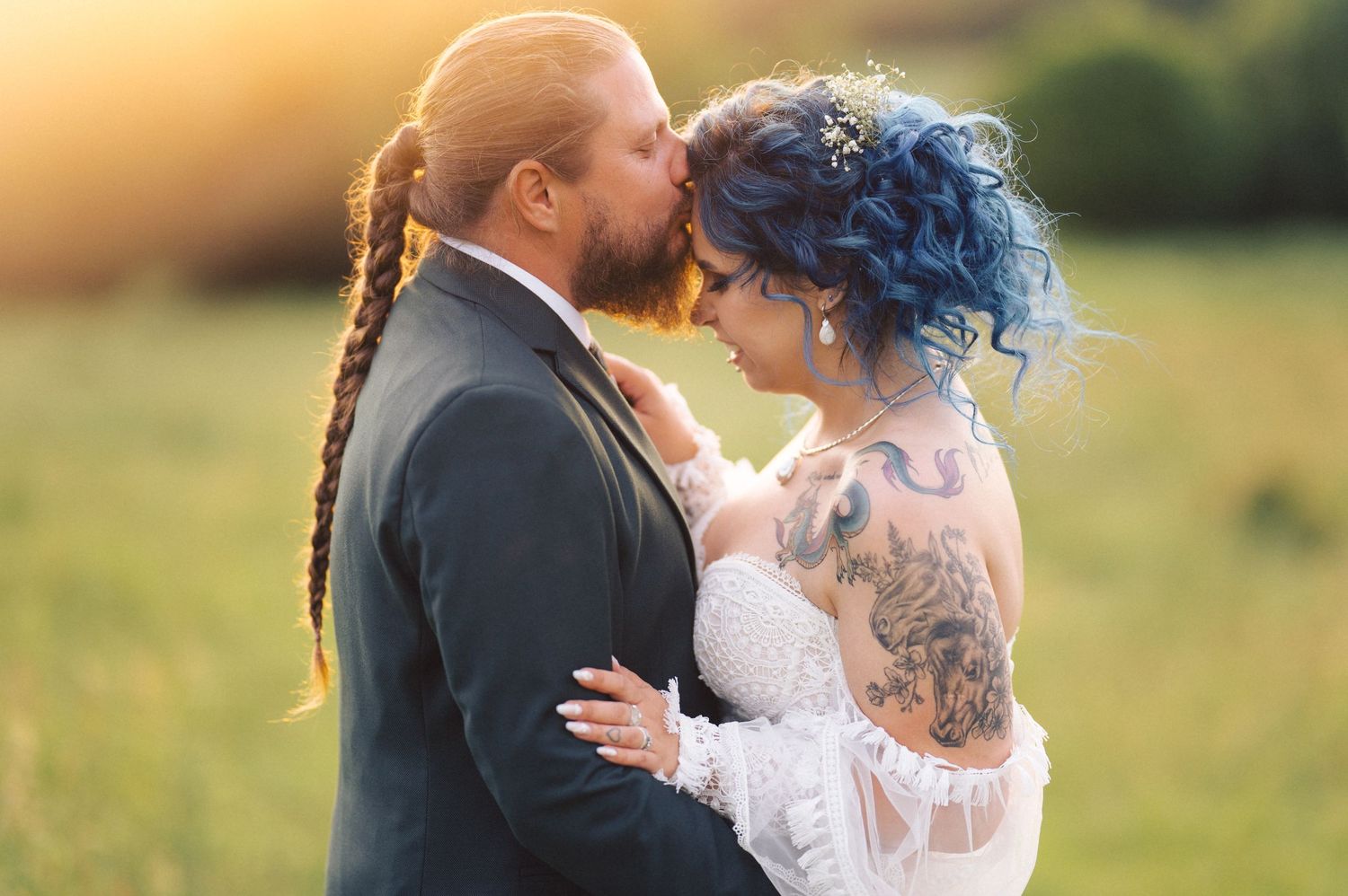 A newly married couple shares a tender moment at sunset in a grassy field, with the bride wearing a lace dress.
