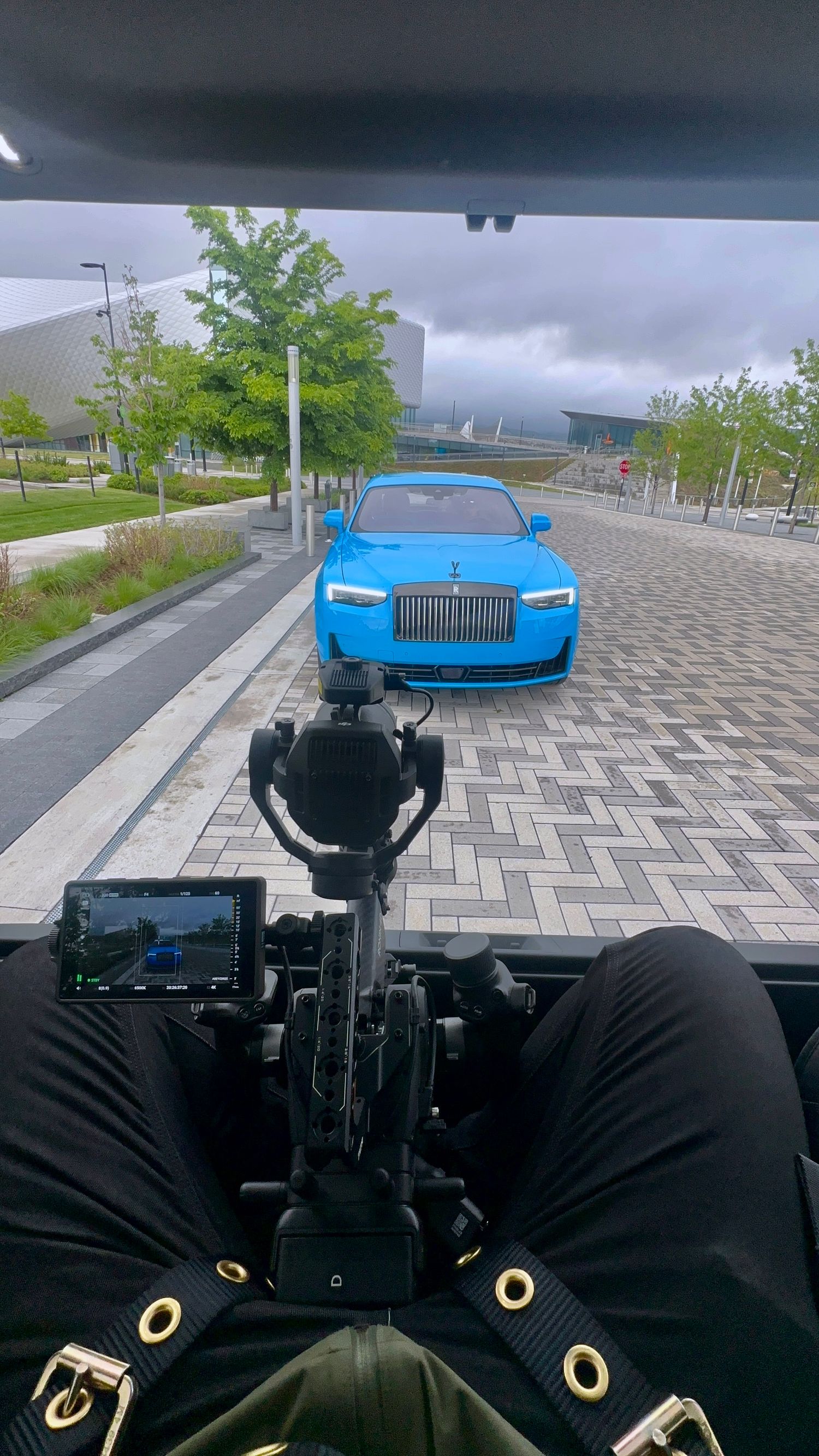 Behind-the-scenes camera filming of a bright blue Rolls-Royce luxury car parked on a patterned brick walkway.