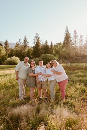 Family group poses together in a golden sunset meadow with tall pine trees in the background. Reno photographer