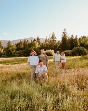 A group stands together in a golden field at sunset with mountains and evergreen trees in the background.