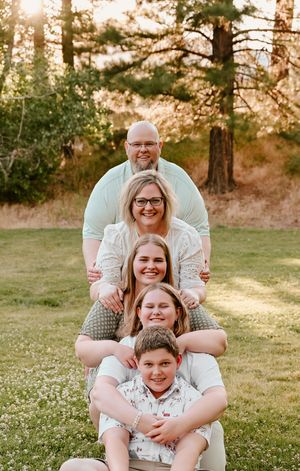 A smiling family in matching light-colored outfits poses together on grassy ground at sunset.