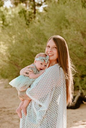 Mother and baby wearing mint green outfits pose together in sunlit outdoor setting with forest backdrop.