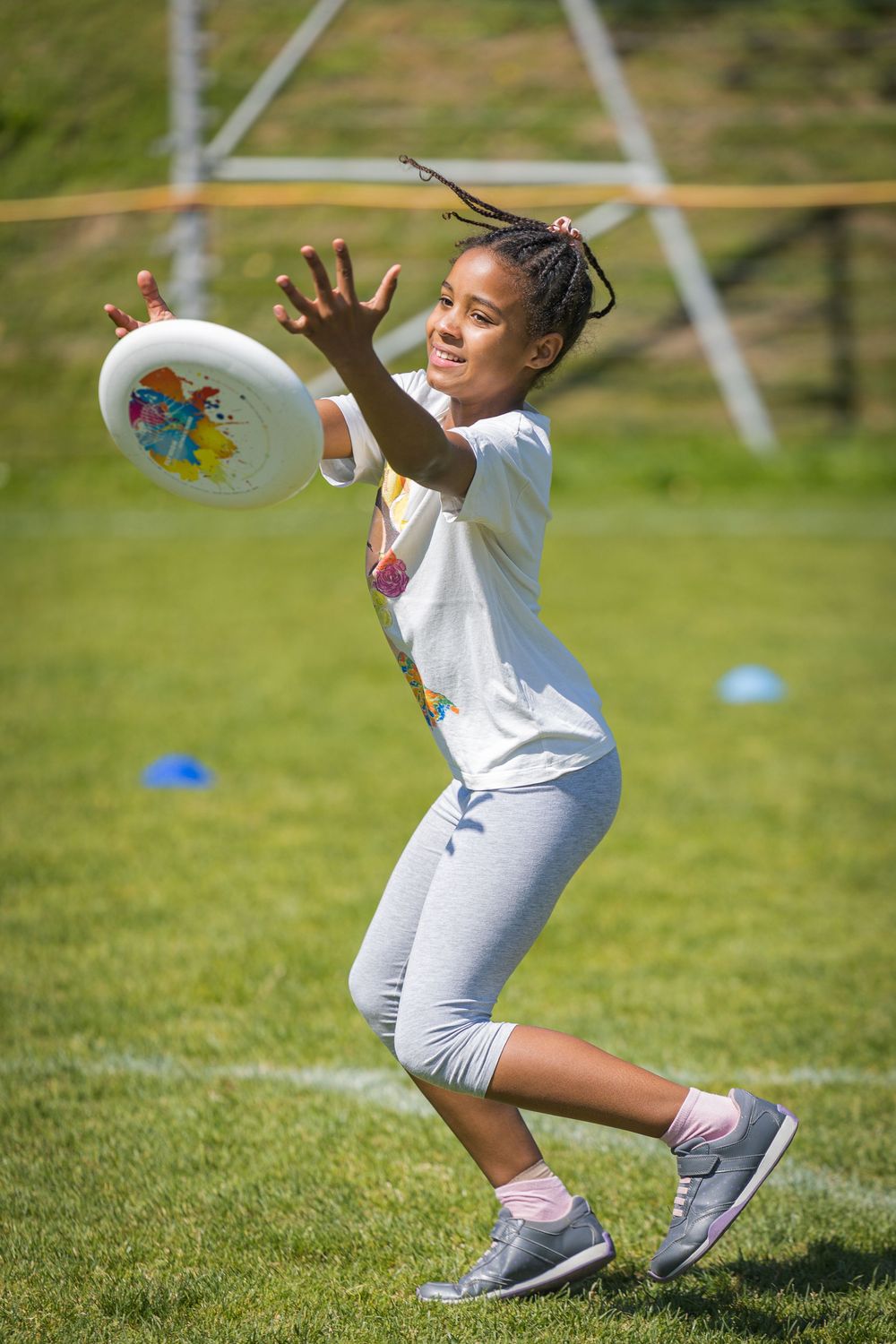 A player reaches to catch a frisbee while playing on a sunny grassy field with powerlines in the background.
