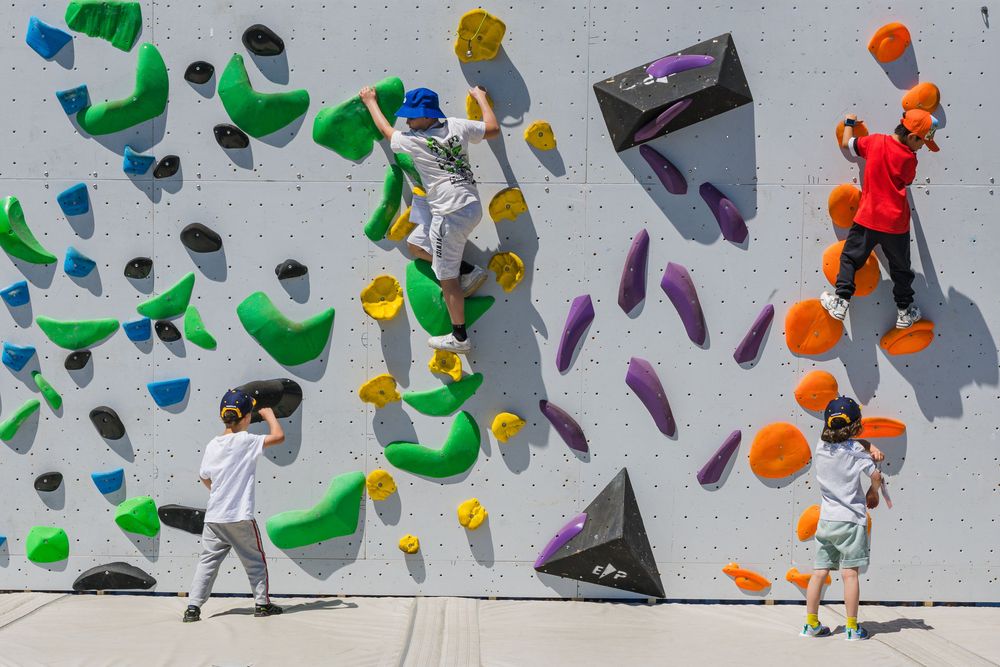Indoor rock climbing wall shown with colorful climbing holds scattered across a grey surface as climbers practice their skills.