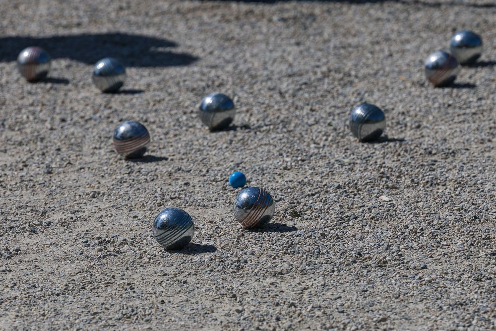 Several petanque or boules balls scattered on a gravel playing surface casting shadows in sunlight.