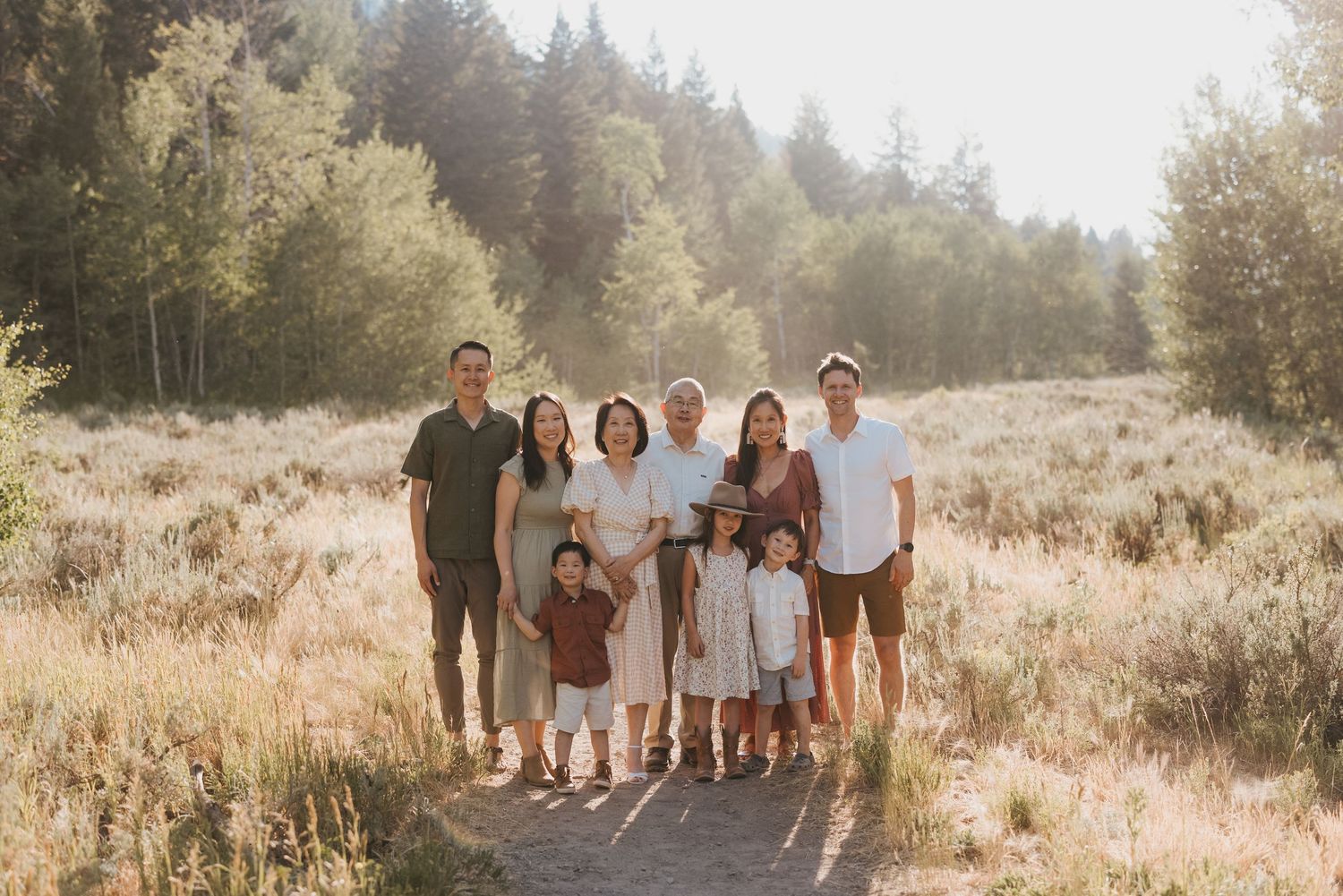 A group portrait standing together on a path in a sun-dappled field with forest in the background.