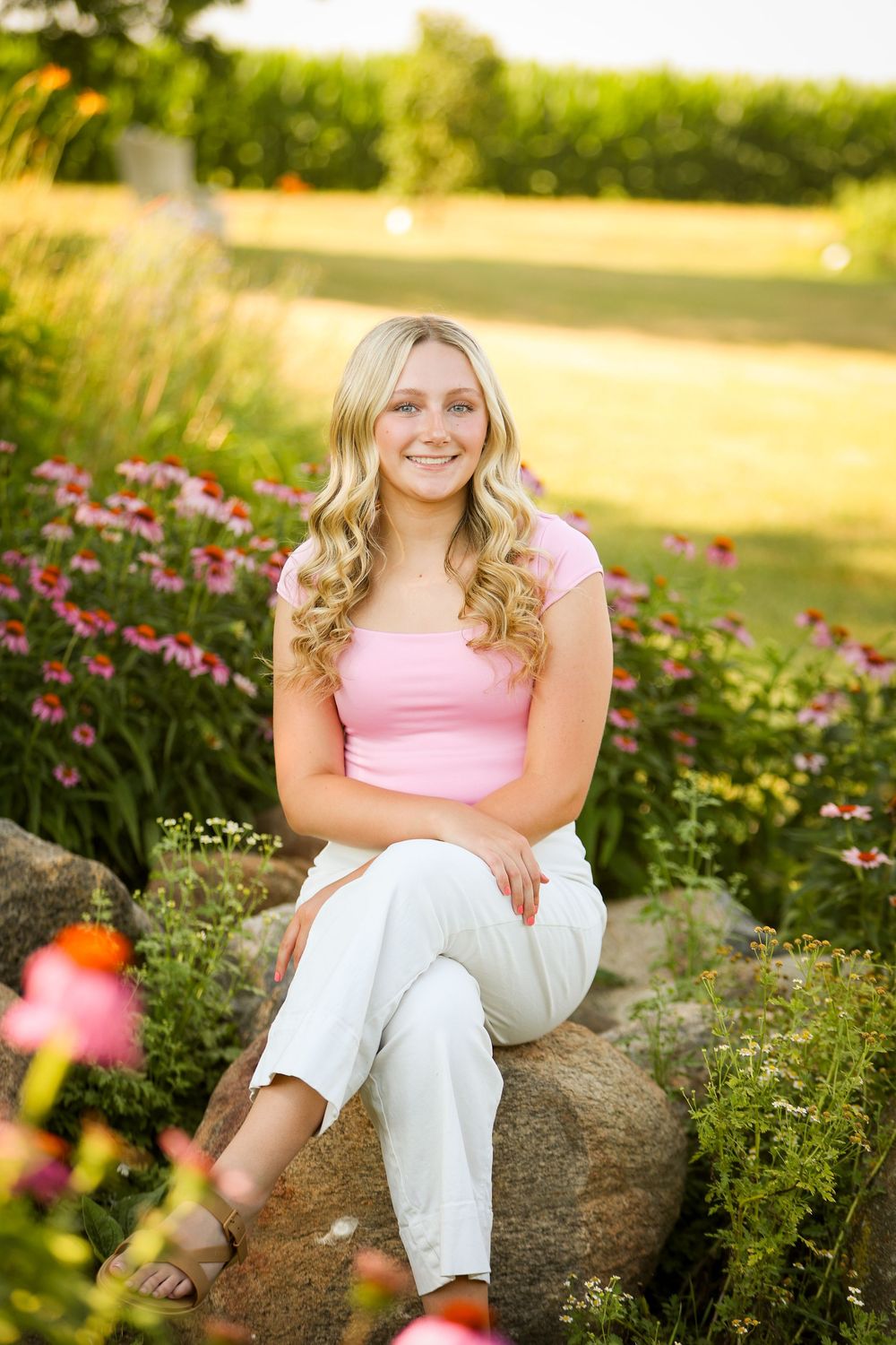 Portrait of person in pink top sitting on rock in garden with pink flowers during golden hour.