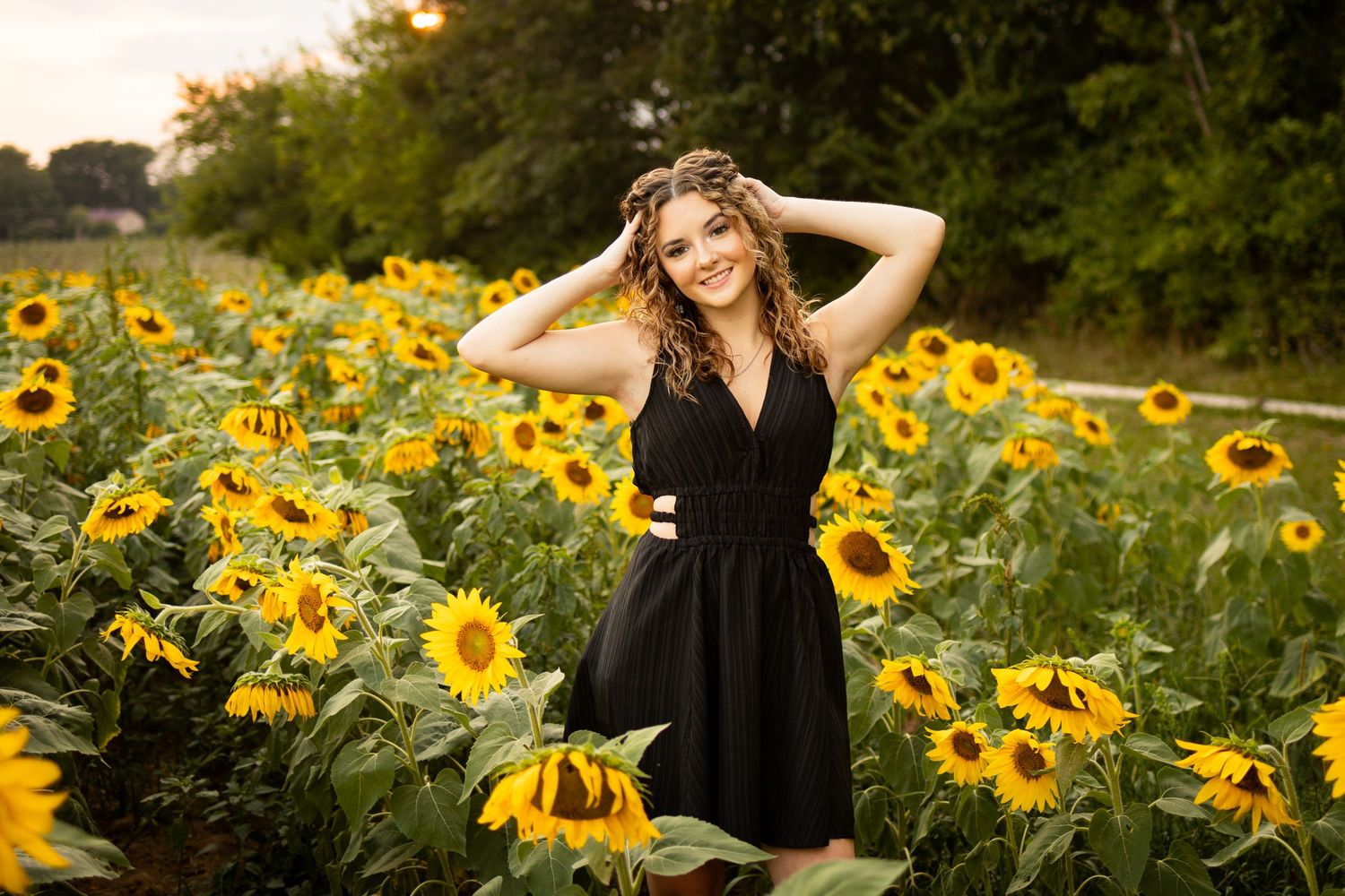 A black sleeveless dress contrasts beautifully against a vibrant field of blooming sunflowers at golden hour.
