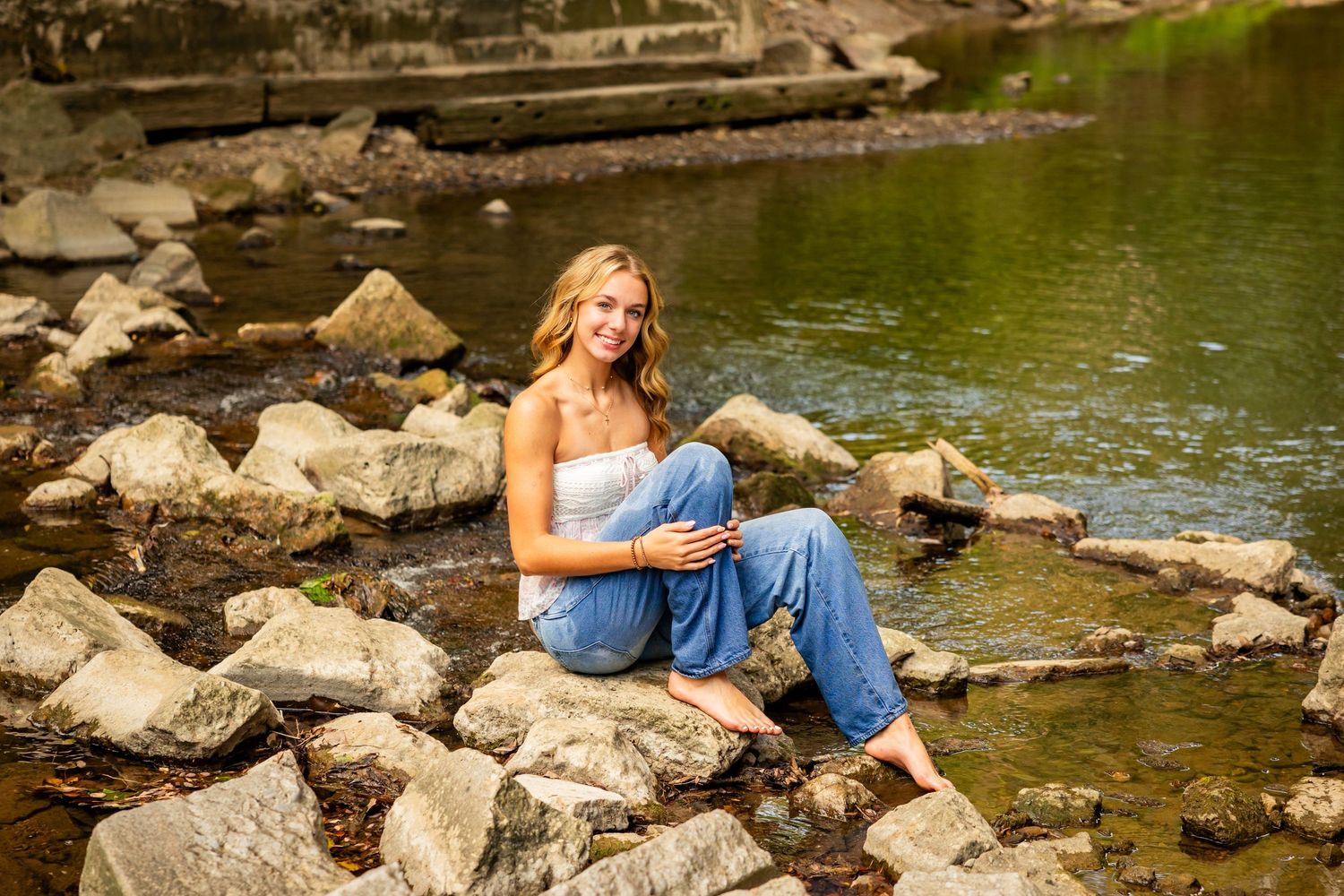 A serene scene by a rocky creek with sunlit water and scattered boulders along the shoreline.