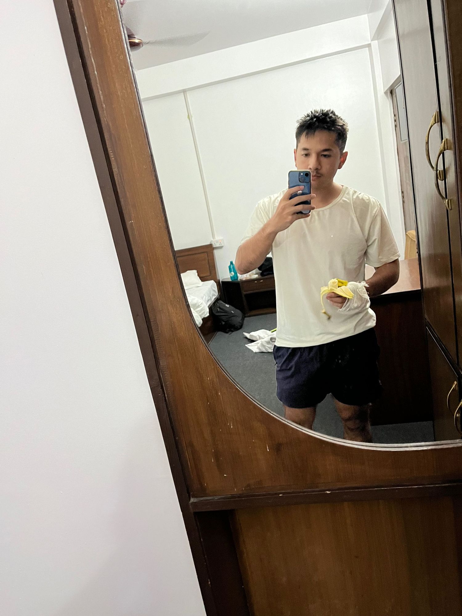 Mirror selfie showing person in white t-shirt and dark shorts.