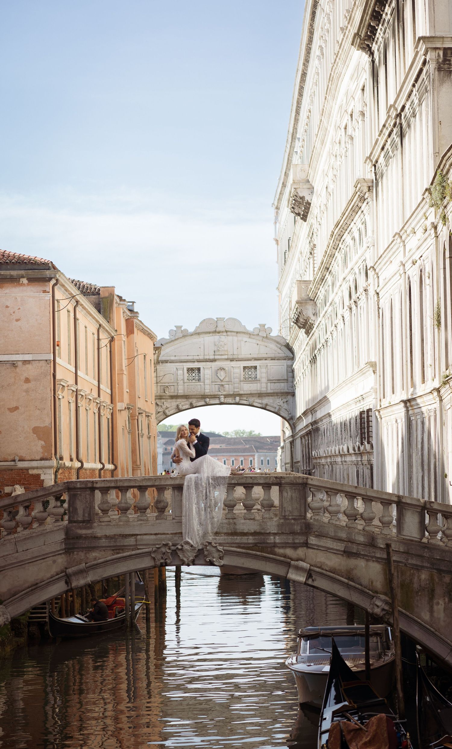 Wedding couple embracing on Bridge of Sighs in Venice with gondolas below.