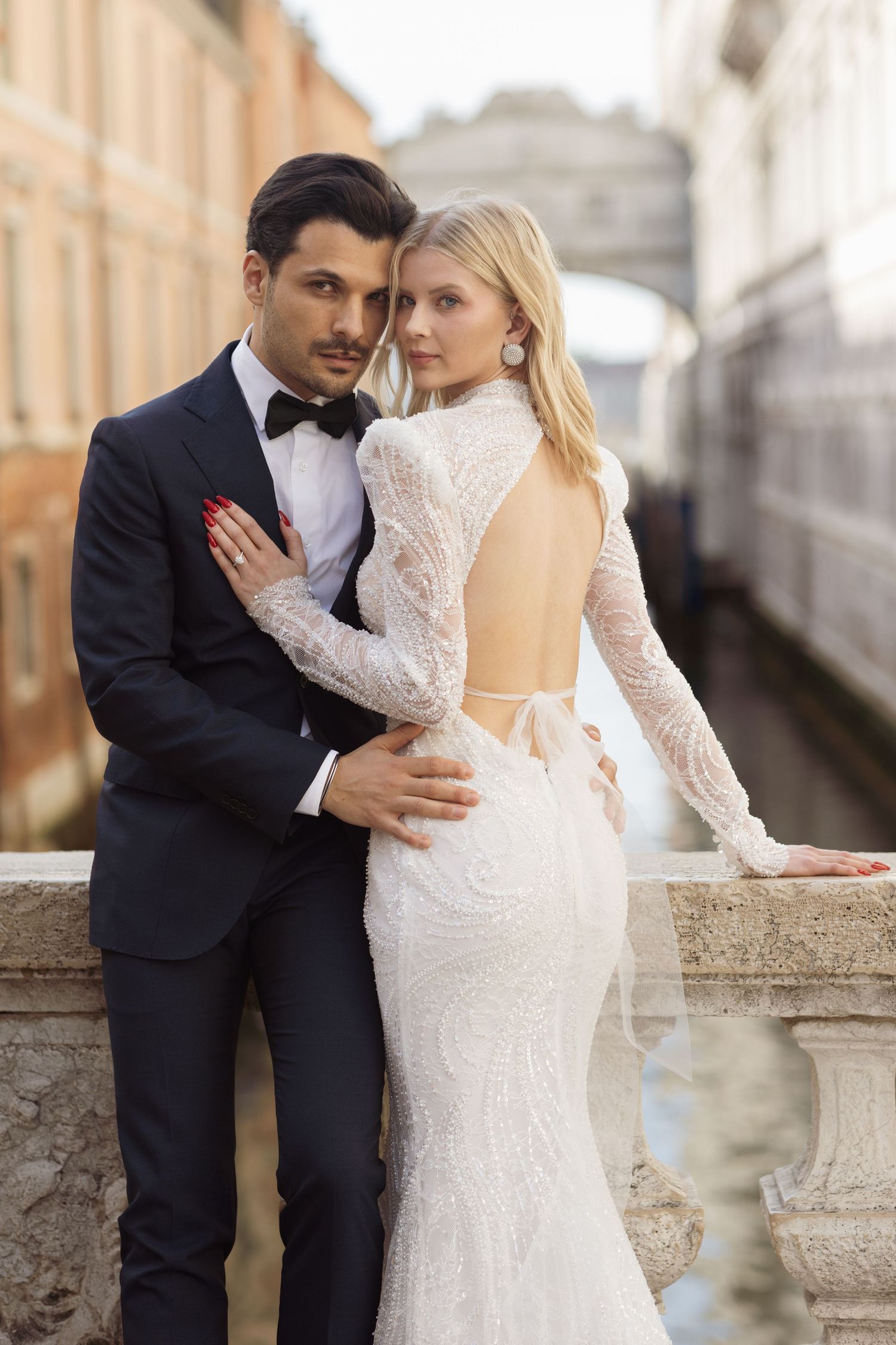 Elegant couple poses on Venice bridge in formal wedding attire.