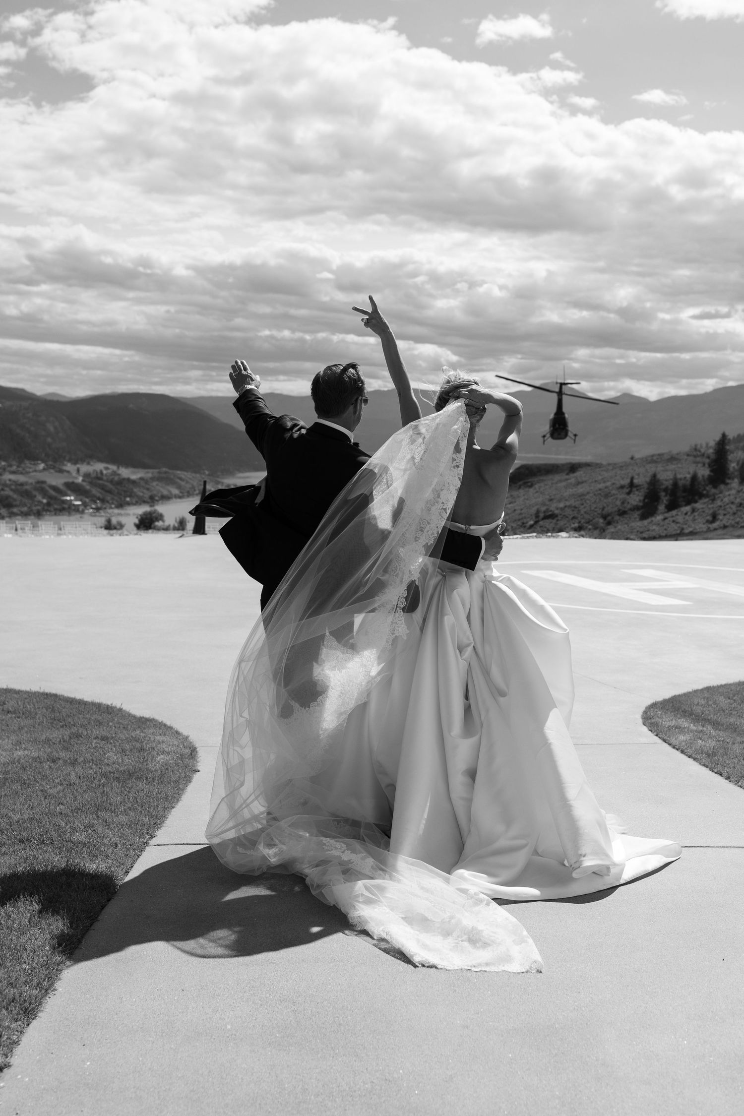 Joyful couple celebrating with raised arms against a mountain landscape backdrop.