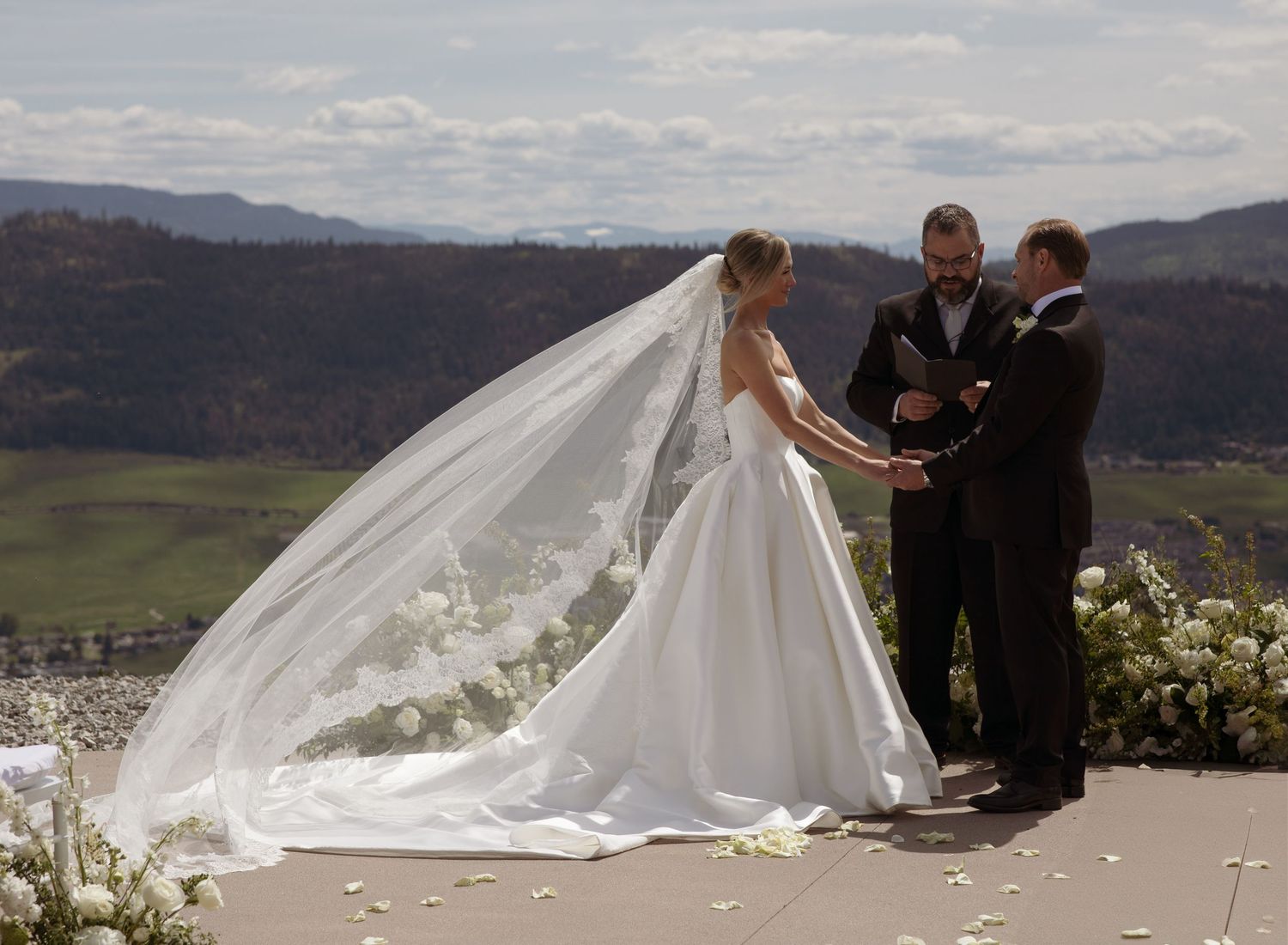 Outdoor wedding ceremony with flowing veil against mountain vista.