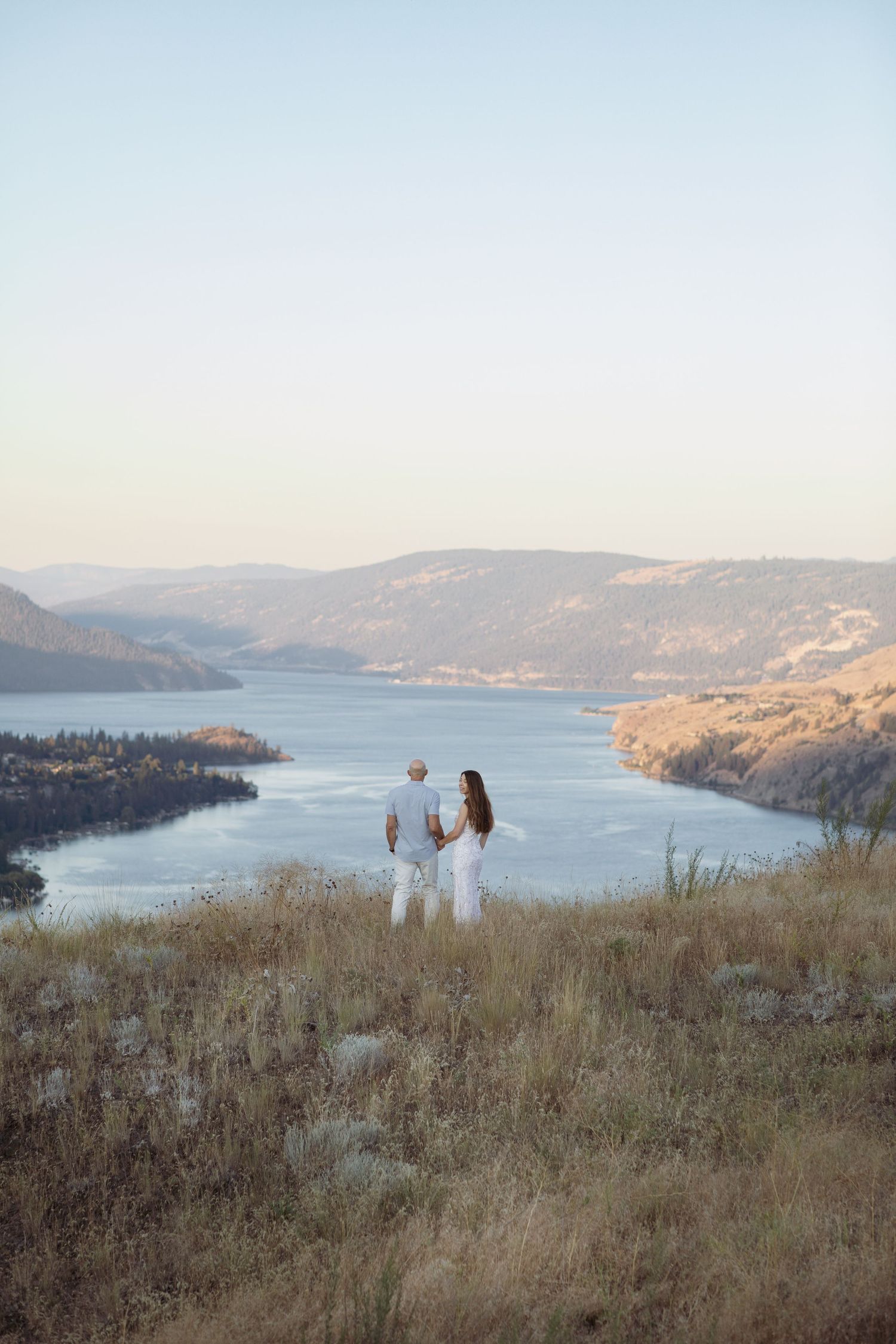 Couple overlooking scenic lake vista from hilltop during sunset.