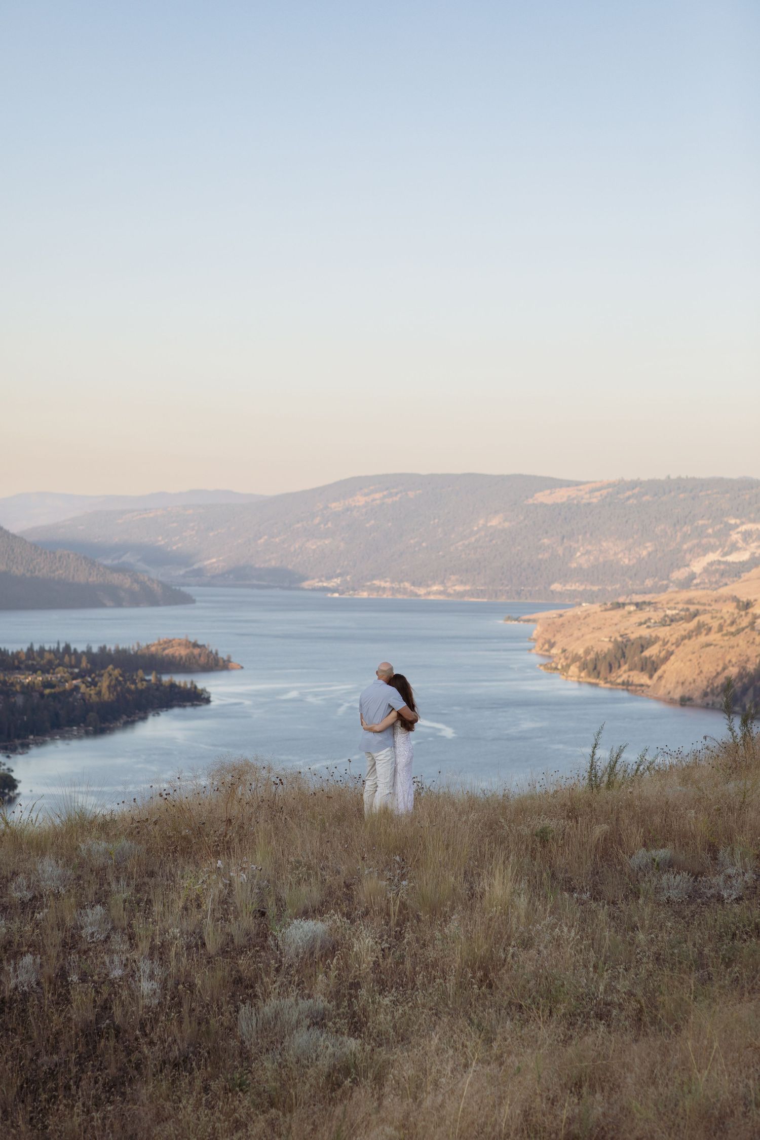 Romantic lift pose against dramatic lake and mountain landscape at dusk.