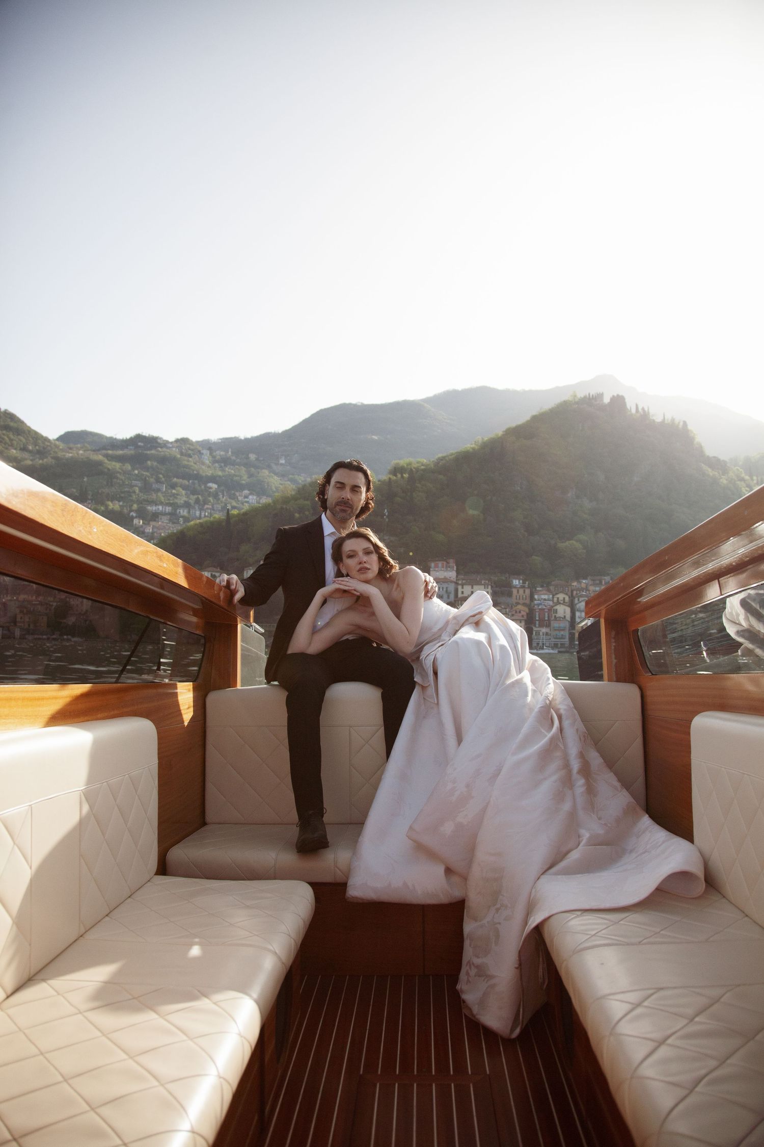 Newlyweds relaxing on luxury wooden boat with mountain scenery.