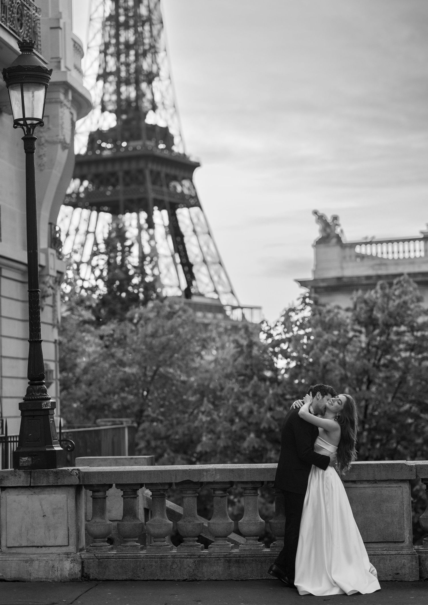 Romantic wedding couple embraces against iconic Eiffel Tower backdrop in black and white Paris setting.