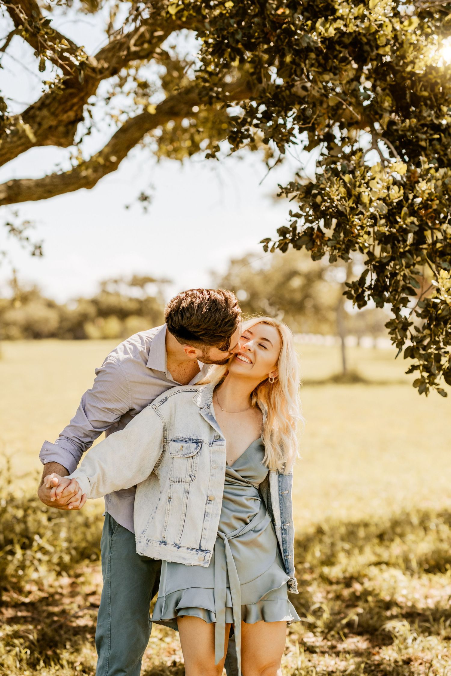 Couple sharing tender moment under oak tree during golden hour.