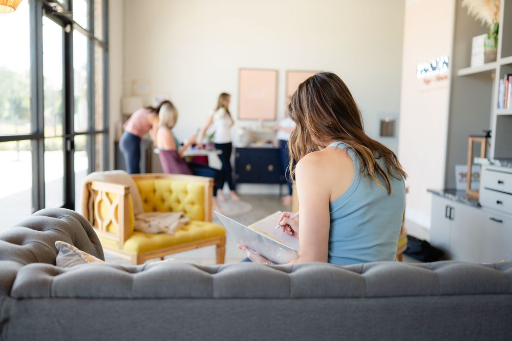 Person sitting on a gray couch reading while others socialize in the background of a modern living room.