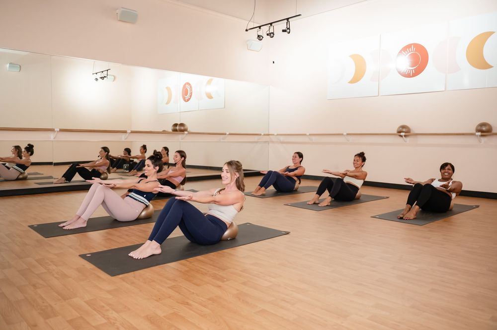 Yoga students performing floor exercises in a spacious studio with moon phase artwork on walls.