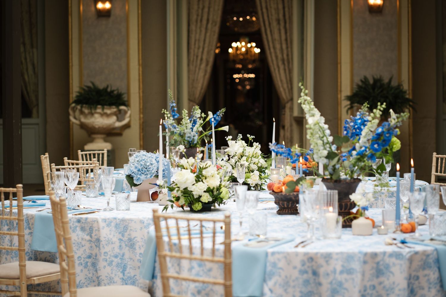 Elegant wedding reception tables decorated with blue and white linens, floral centerpieces, and gold chiavari chairs.