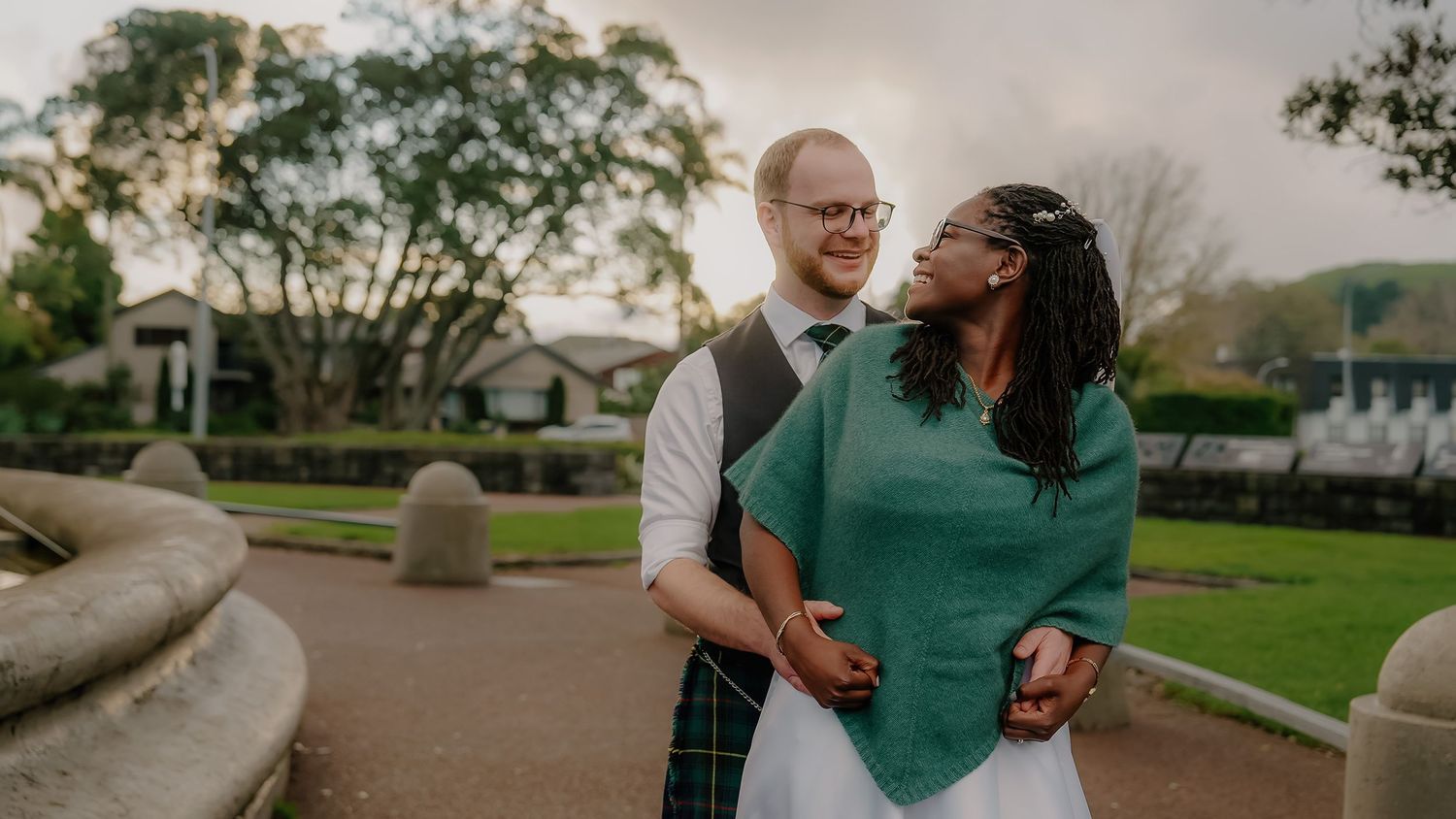 A romantic couple shares a joyful embrace and laugh together in a park at sunset.