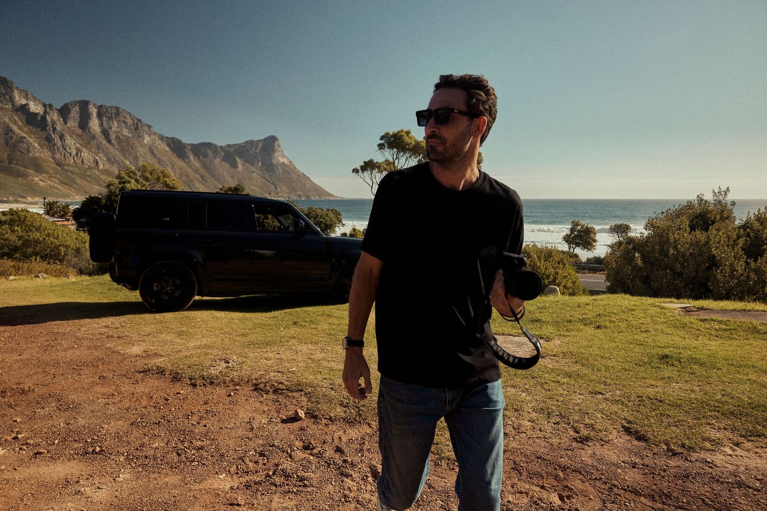 Outdoor scene showing someone holding camer on a scenic coastal viewpoint in Cape Town with rugged mountains and ocean in background.