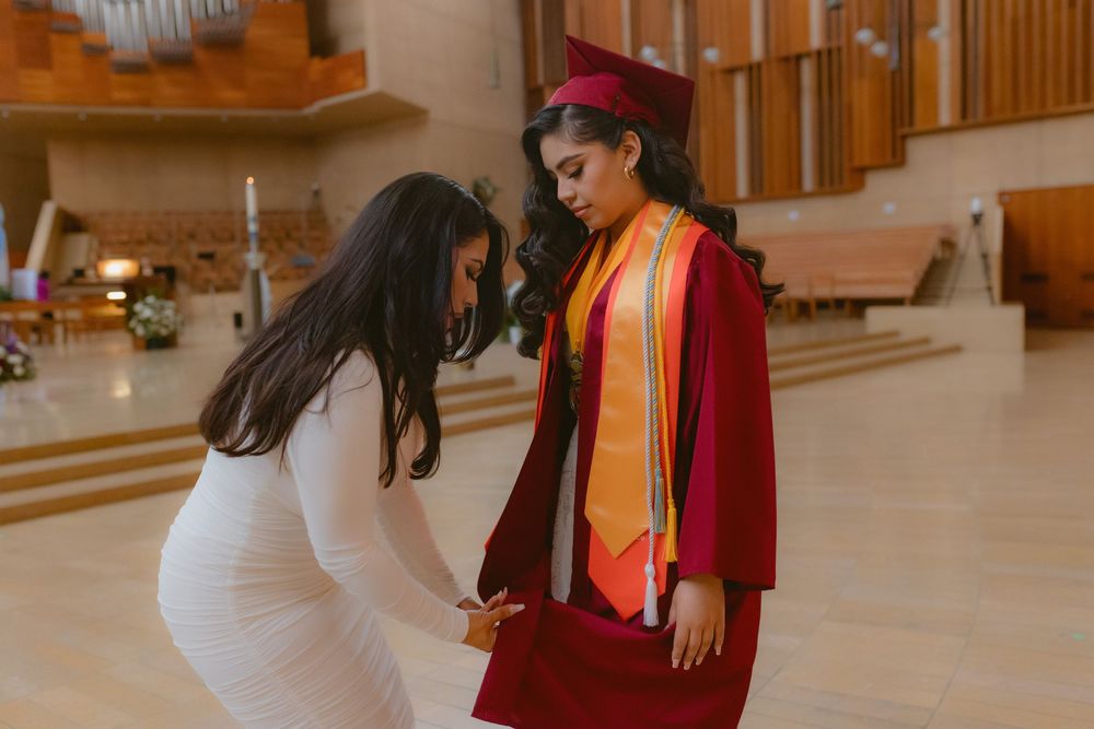 Two people share a joyful moment in a wood-paneled indoor space with one wearing a red graduation gown and stole.