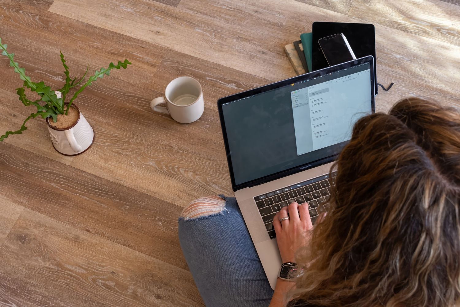 Overhead view of laptop computer with coffee cup and small plant on wooden desk during remote work session.