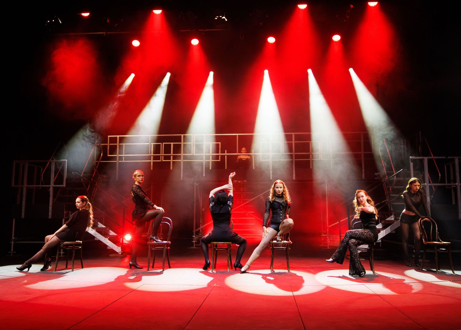 Dramatic dance performance on stage with red spotlights creating silhouettes during live theatrical show.