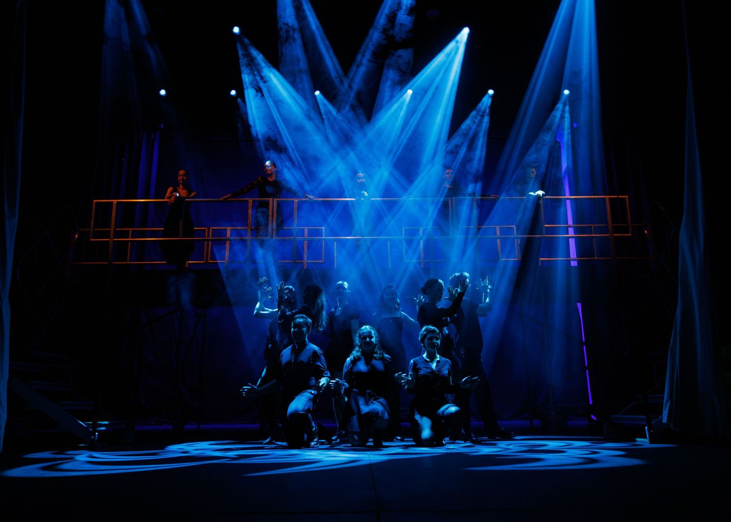 Performers silhouetted on stage under dramatic blue spotlights during a theatrical production.