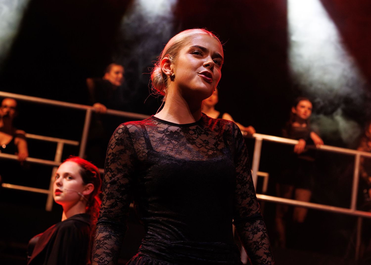 A performer sings passionately on stage during a theatrical production while wearing a dark lace costume.
