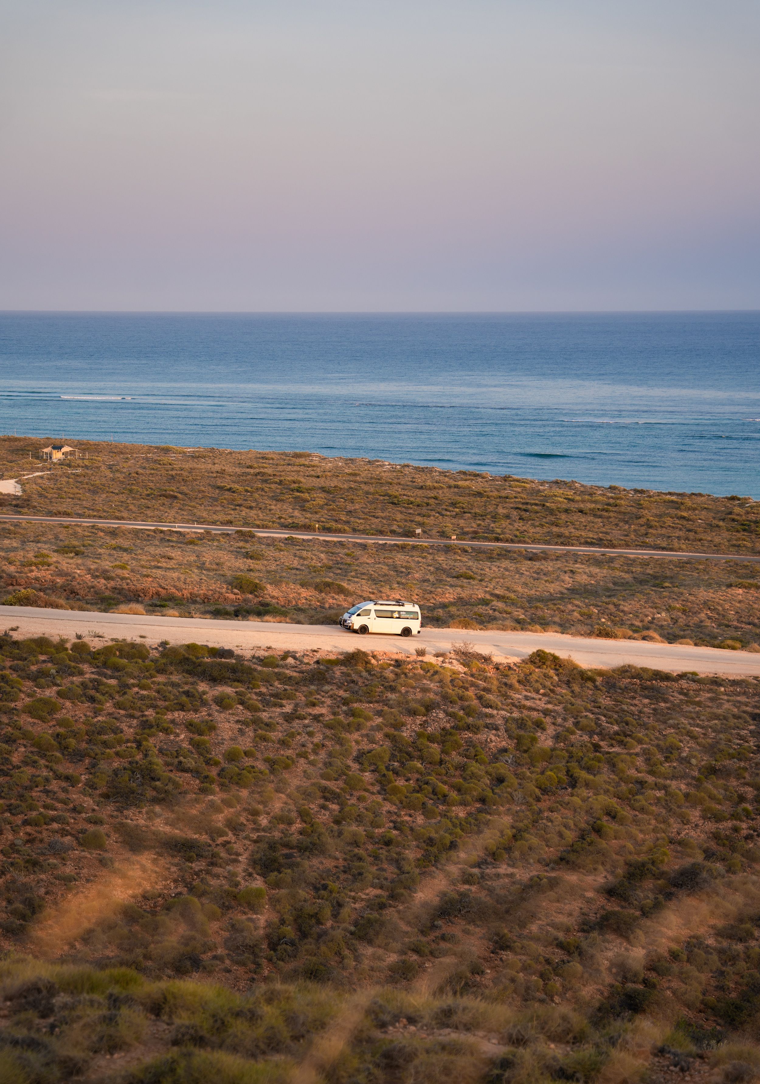 Aerial view of a white van traversing coastal terrain with ocean views.