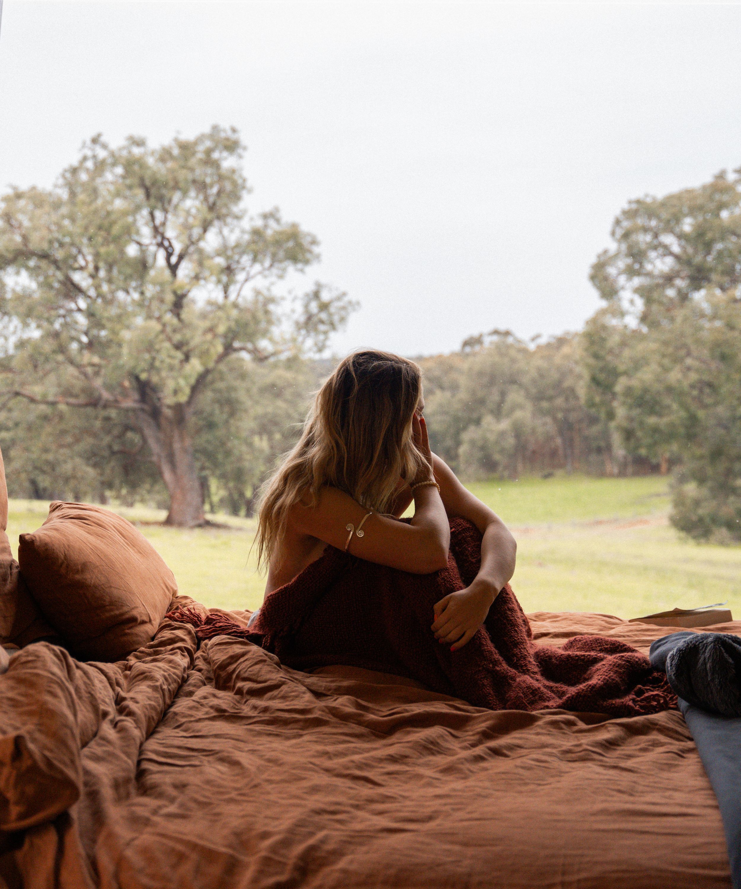 Comfortable bedding arrangement inside a camper van with rural views.