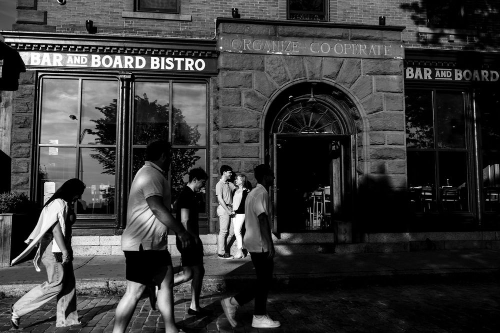 Restaurant storefront for Board Bistro captured in moody black and white with people walking past.