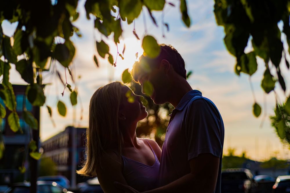 Romantic silhouette of a couple sharing an intimate moment at sunset with leaves framing the scene.